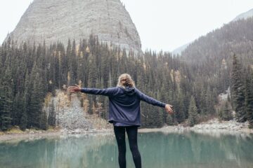 Image of lady with arms up in the air in front of hill and lake