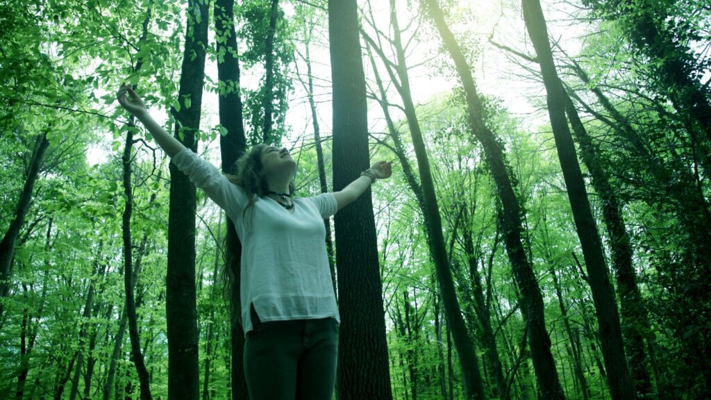 Feeling spark of happiness in the woods, lifting arms in the air