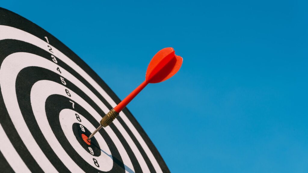 Dart board with arrow in bull to indicate hitting target.