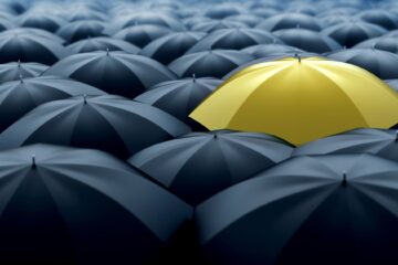 Yellow Umberella standing out from black umberellas signifying standing out and up