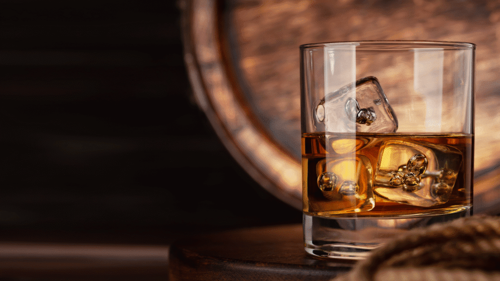 whiskey glass filled with whiskey and ice in front of a barrel